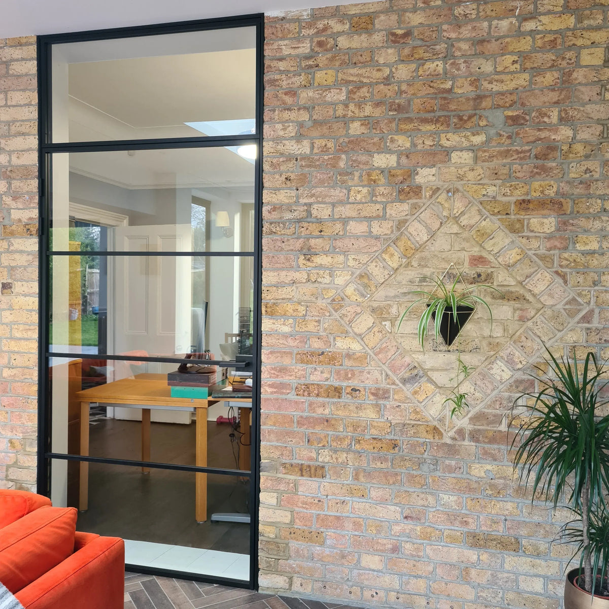 Black-framed glass partition in modern home with exposed brick wall and indoor plants