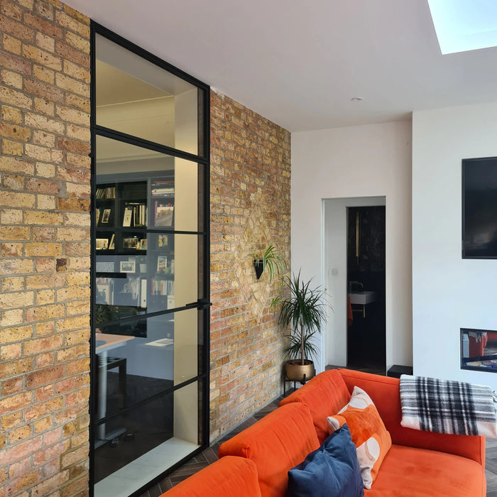 Black-framed glass partition in modern living room with exposed brick wall and orange sofa