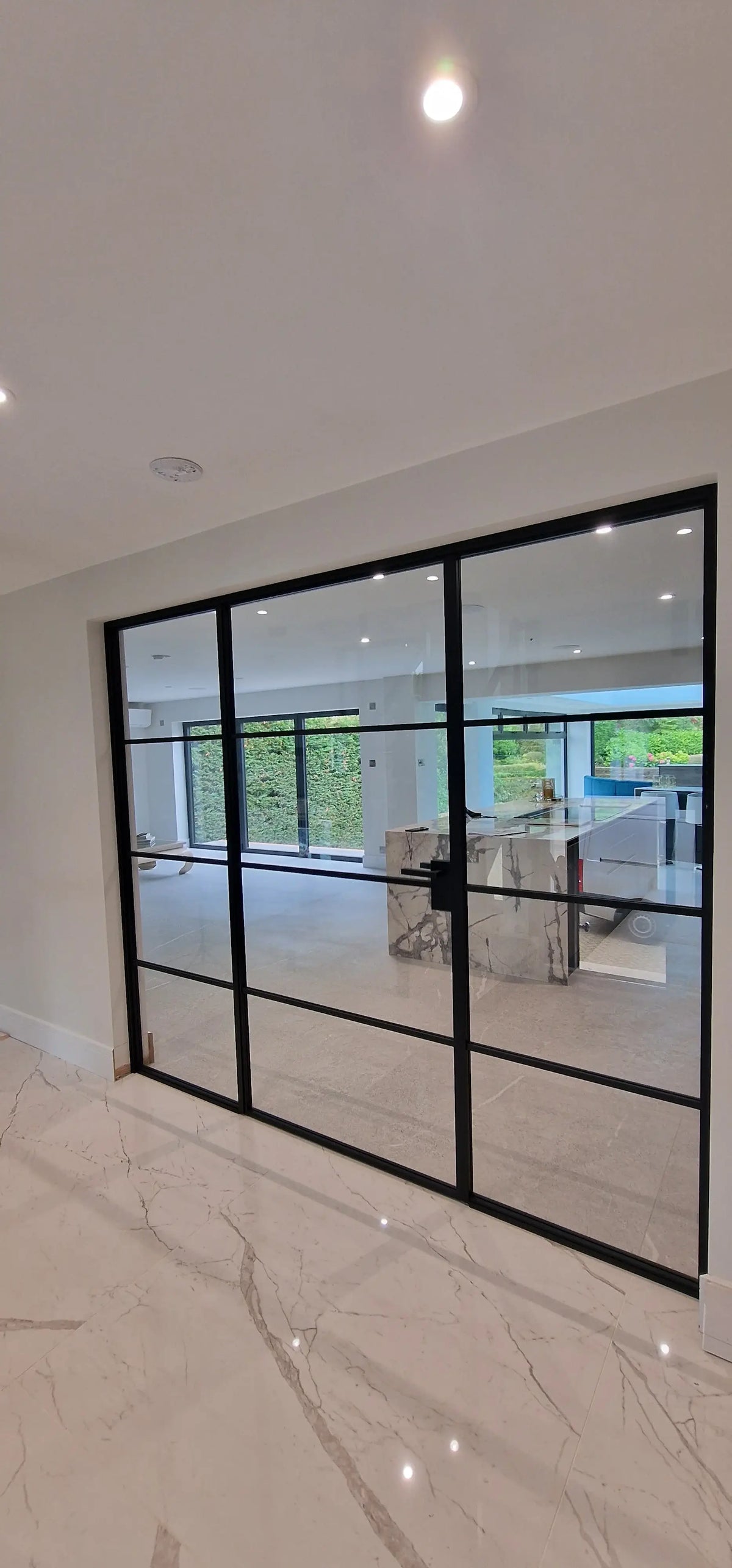 Black-framed glass partition with grid design in modern luxury home, showcasing sleek interior and marble flooring.