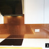 Modern kitchen with orange fine glitter glass splashback, white cabinets, black cooktop, and range hood