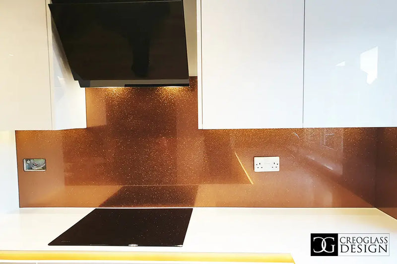 Modern kitchen with orange fine glitter glass splashback, white cabinets, black cooktop, and range hood