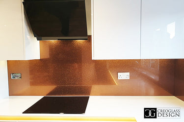 Modern kitchen with orange fine glitter glass splashback, white cabinets, black cooktop, and range hood