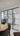 Modern interior with black framed double glass doors and side panels separating dining area with wooden round table and black chairs from staircase.