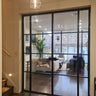 Modern black metal double door with side panels opening to a bright living room with beige sofas and wooden floor
