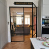 Modern kitchen with white cabinets and double hinged black metal frame glass door leading to living room