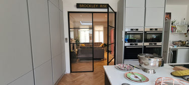 Modern kitchen with white cabinets and double hinged black metal frame glass door leading to living room