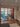 Modern living room with black framed glass double doors opening to dining area featuring wooden floors