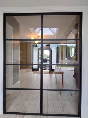 modern black double hinged steel framed glass door in bright spacious interior with wood flooring