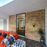 Modern interior with exposed brick wall, black framed glass door, orange sofa, and chess table