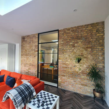Modern interior with exposed brick wall, black framed glass door, orange sofa, and chess table