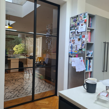 Black double hinged glass door with frame leading to a living space, adjacent to refrigerator with photos and notes