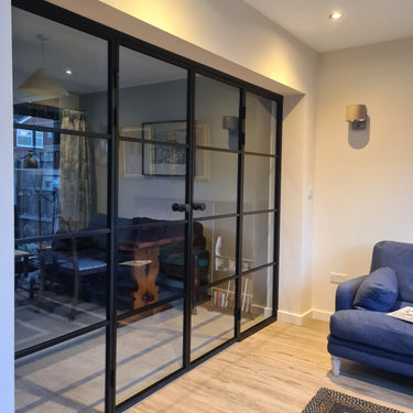 Modern double glass door with black frame and side panels separating two living spaces