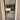 Modern black framed glass hinged door with white trim showing view into living room with beige sofa and wooden flooring