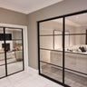Modern interior with black framed double hinged glass doors separating two living rooms with beige sofas