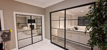 Modern interior with black framed double hinged glass doors separating two living rooms with beige sofas