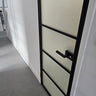 Modern hinged door with black metal frame and frosted glass panels in a minimalist white hallway