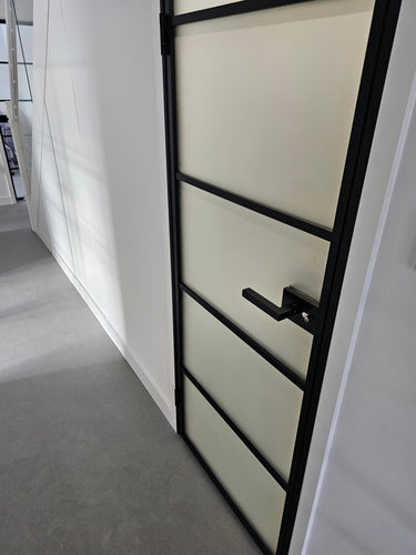 Modern hinged door with black metal frame and frosted glass panels in a minimalist white hallway