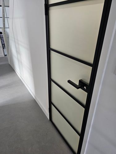 Modern hinged door with black metal frame and frosted glass panels in a minimalist white hallway