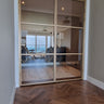 Double hinged glass doors with gold frame and handles leading to a living room with sea view