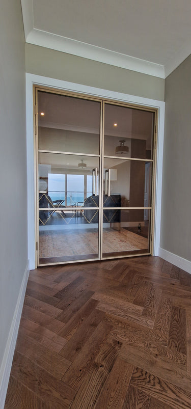 Double hinged glass doors with gold frame and handles leading to a living room with sea view