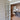 Interior view of a double hinged glass door with bronze frame opening into a room with herringbone wood flooring and modern decor