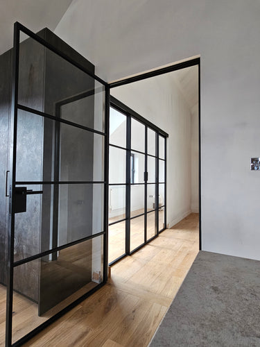 Modern interior with black-framed glass hinged door and light wood flooring