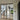 Black framed double hinged glass doors separating modern interior with wooden stairs and outdoor green view