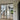 Black framed double hinged glass doors separating modern interior with wooden stairs and outdoor green view