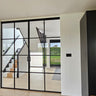 double hinged black metal framed glass doors partitioning a bright room with wooden stairs and light wood flooring