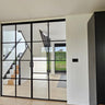 double hinged black metal framed glass doors partitioning a bright room with wooden stairs and light wood flooring