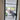 Black framed glass hinged door opening into modern living space with gray chairs and potted plants