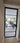 Black framed glass hinged door opening into modern living space with gray chairs and potted plants