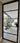 Black metal framed glass hinged door showing modern indoor patio with large plant and purple sofa