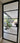 Black metal framed glass hinged door showing modern indoor patio with large plant and purple sofa
