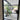 Black framed glass hinged door opening to modern patio with potted plant and outdoor seating