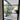 Black framed glass hinged door opening to modern patio with potted plant and outdoor seating
