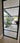 Black framed glass hinged door opening to modern patio with potted plant and outdoor seating