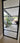 Black framed glass hinged door opening to modern patio with potted plant and outdoor seating