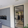 Modern kitchen with gray cabinets and a black-framed glass hinged door leading to another room