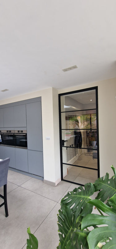 Modern kitchen with gray cabinets and a black-framed glass hinged door leading to another room