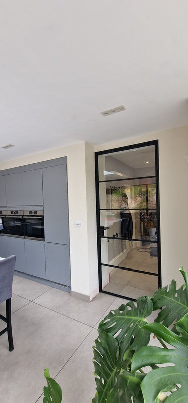 Modern kitchen with gray cabinets and a black-framed glass hinged door leading to another room