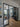 Modern black metal double doors with glass panels opening to cozy living room with leather armchair and round mirror