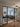 Modern black framed glass double doors with two side panels opening into a cozy living room with a gray sectional sofa and patterned rug