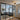 Modern interior with black steel-framed double glass door and side panels separating living room featuring grey sectional sofa and patterned rug
