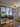 Modern interior with black steel-framed double glass door and side panels separating living room featuring grey sectional sofa and patterned rug