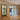 Double black metal frame glass doors with two side panels separating wooden floor room and tiled kitchen
