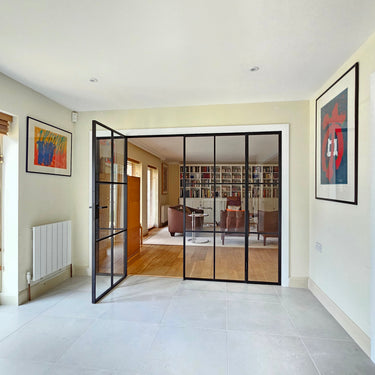 Modern black metal framed double doors with side panels separating tiled room from cozy living room with bookshelves