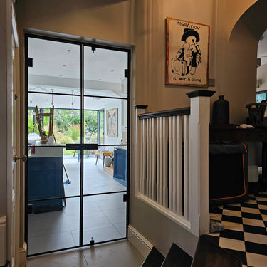 Interior view of black metal-framed glass double hinged door leading to bright kitchen with blue cabinets and garden
