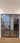 Double hinged black metal frame glass door in modern home entryway with wood tile floor