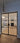 Modern double hinged black frame glass doors opening to elegant living room with fireplace and chandelier